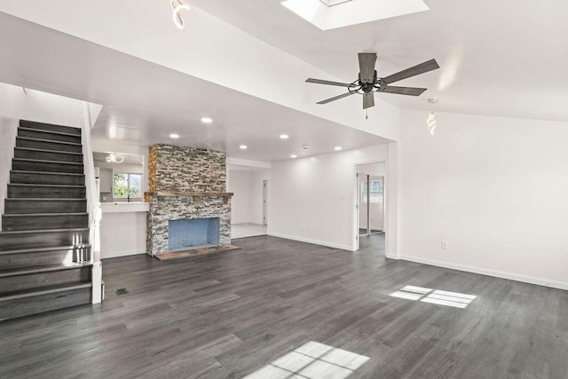 unfurnished living room featuring ceiling fan, dark wood-type flooring, vaulted ceiling with skylight, and a stone fireplace