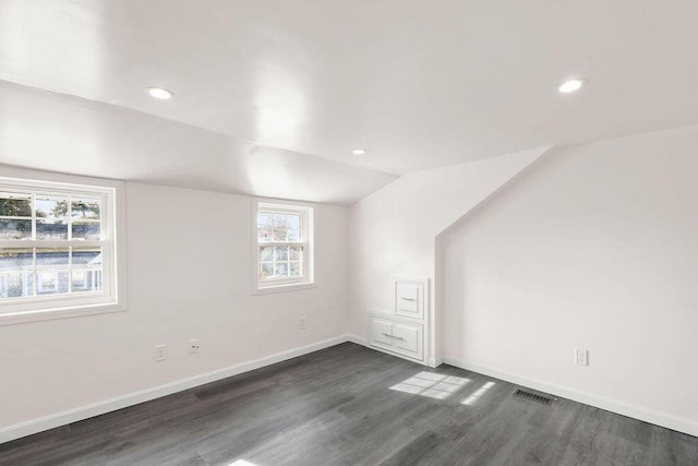 additional living space featuring dark hardwood / wood-style flooring, a healthy amount of sunlight, and vaulted ceiling