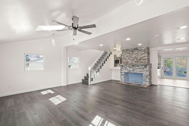 unfurnished living room with ceiling fan, lofted ceiling with skylight, dark hardwood / wood-style floors, and a stone fireplace