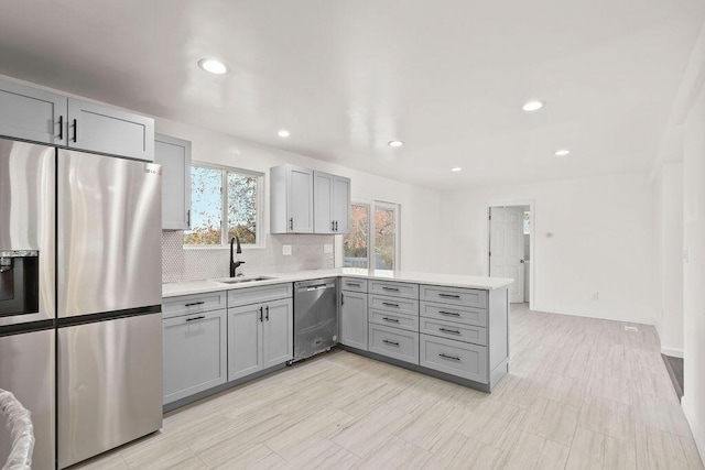 kitchen featuring stainless steel appliances, decorative backsplash, sink, gray cabinets, and kitchen peninsula