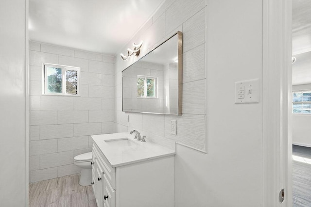 bathroom with plenty of natural light, tile walls, toilet, and vanity