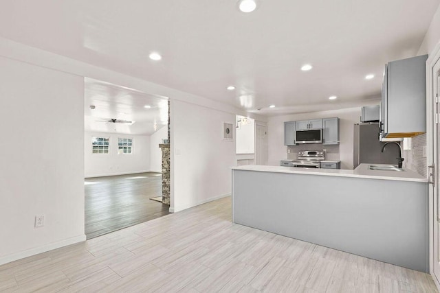 kitchen with kitchen peninsula, ceiling fan, appliances with stainless steel finishes, sink, and gray cabinetry