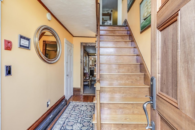 staircase with wood-type flooring, ornamental molding, and a textured ceiling