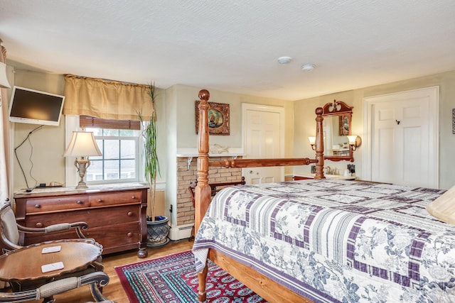 bedroom featuring a textured ceiling, a baseboard heating unit, and light hardwood / wood-style flooring