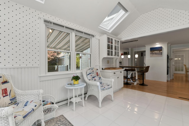 interior space with a baseboard heating unit, light tile patterned floors, and lofted ceiling with skylight