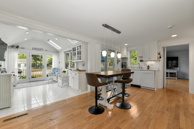 kitchen featuring dishwasher, white cabinets, decorative light fixtures, light hardwood / wood-style flooring, and vaulted ceiling