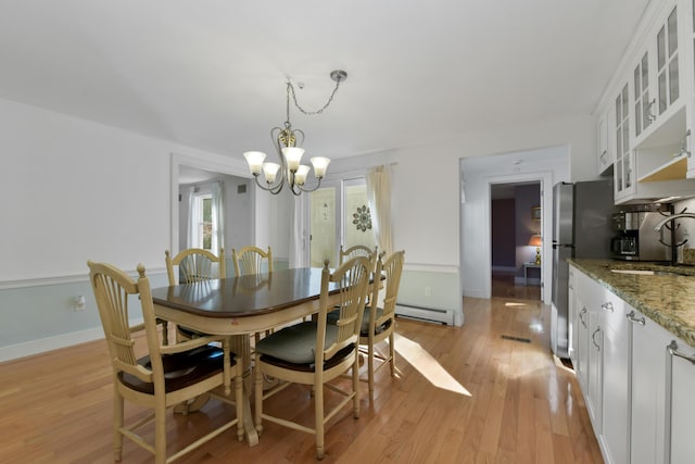 dining space with a baseboard radiator, sink, a notable chandelier, and light wood-type flooring