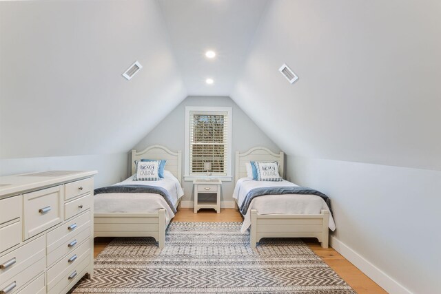 bedroom featuring light wood-style flooring, baseboards, vaulted ceiling, and visible vents