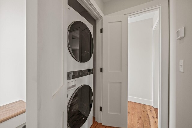 clothes washing area with stacked washing machine and dryer and light wood-type flooring