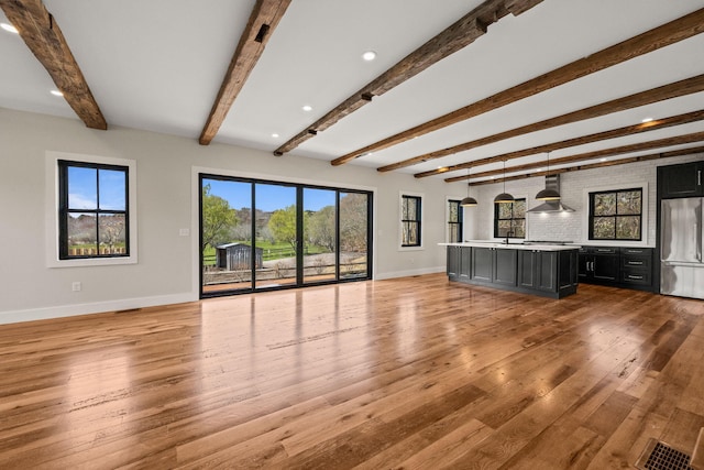 unfurnished living room with baseboards, light wood-style flooring, beamed ceiling, and a sink