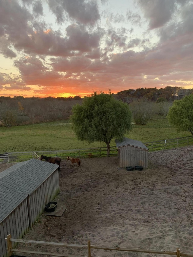 yard at dusk with a view of rural / pastoral area, an outdoor structure, a storage shed, and fence