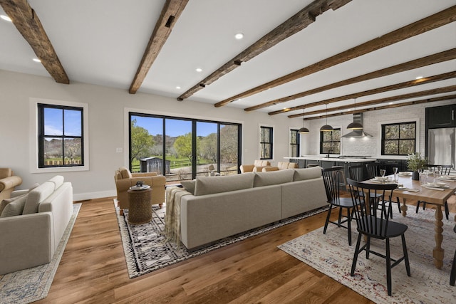 living area with baseboards, beamed ceiling, and light wood-style floors