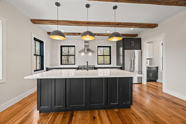 kitchen featuring freestanding refrigerator, wall chimney exhaust hood, dark cabinetry, baseboards, and light wood-type flooring