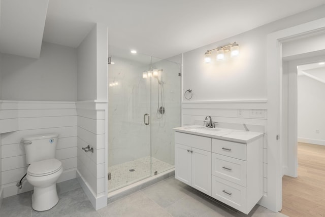 full bathroom featuring wainscoting, toilet, vanity, and a marble finish shower