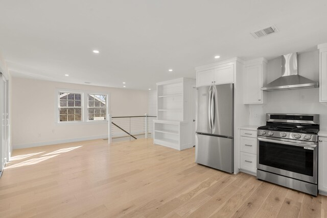 kitchen with appliances with stainless steel finishes, visible vents, light wood-style floors, and wall chimney range hood