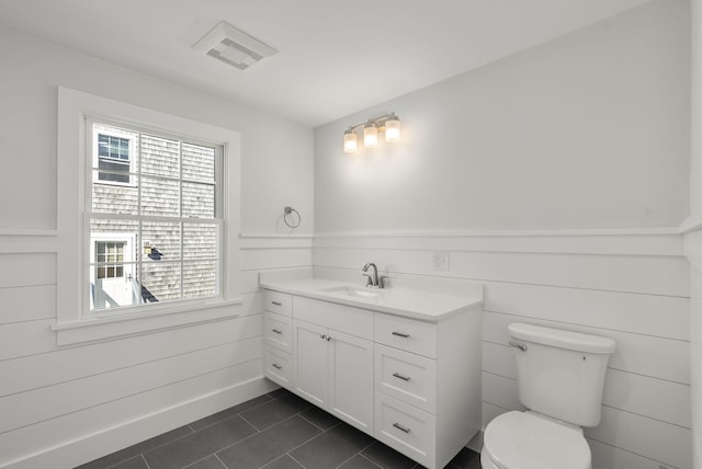 bathroom with visible vents, toilet, a wainscoted wall, tile patterned floors, and vanity