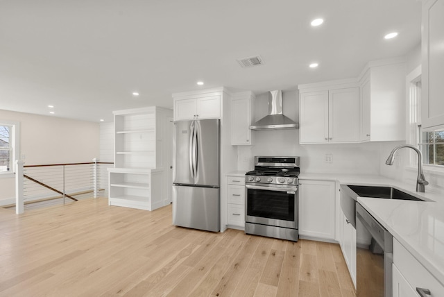 kitchen with stainless steel appliances, a sink, visible vents, white cabinetry, and wall chimney range hood