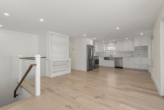 kitchen featuring light wood finished floors, appliances with stainless steel finishes, light countertops, white cabinetry, and a sink