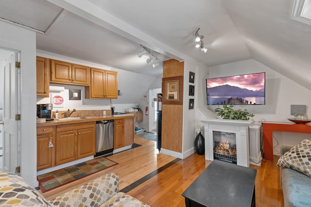 kitchen with sink, stainless steel dishwasher, light wood-type flooring, and lofted ceiling