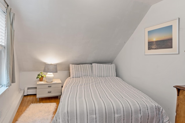 bedroom featuring light hardwood / wood-style floors, a baseboard heating unit, and vaulted ceiling