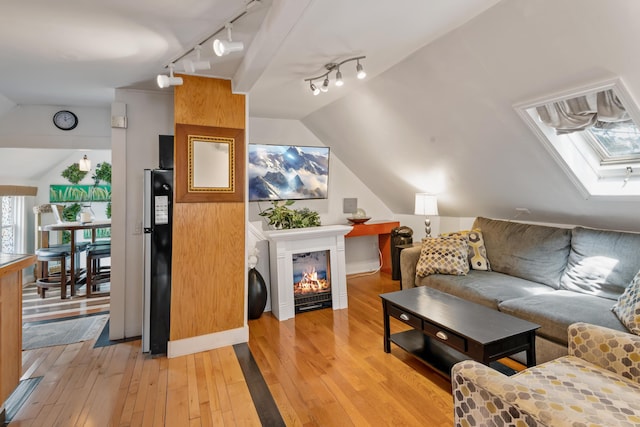 living room with rail lighting, light wood-type flooring, and vaulted ceiling with skylight