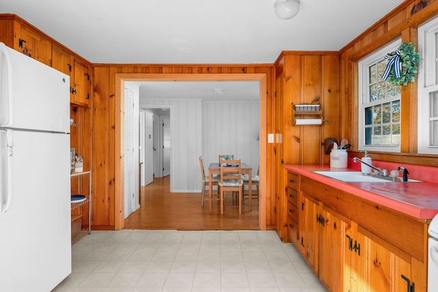 kitchen with sink, white refrigerator, wooden walls, and stove