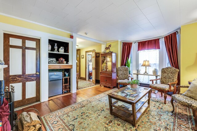 living room featuring built in shelves, ornamental molding, and hardwood / wood-style flooring