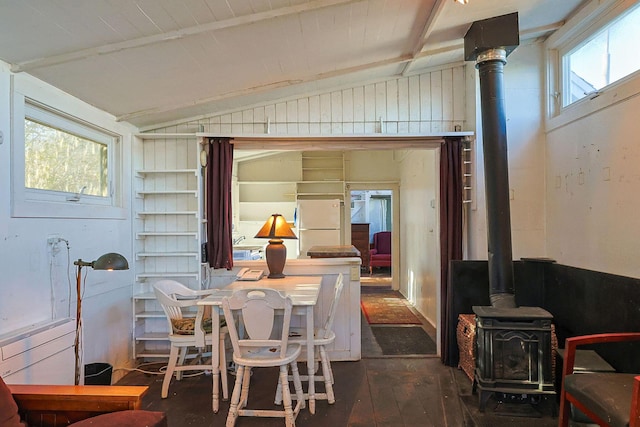 dining area featuring lofted ceiling, wood walls, dark wood-type flooring, and a wood stove