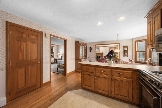 kitchen with a textured ceiling, range, decorative light fixtures, light hardwood / wood-style floors, and kitchen peninsula