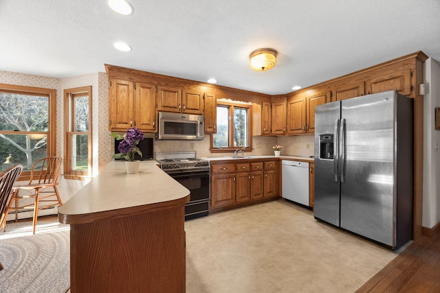 kitchen featuring sink, baseboard heating, kitchen peninsula, and appliances with stainless steel finishes