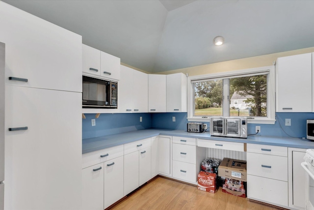 kitchen with lofted ceiling, black microwave, light countertops, and light wood finished floors