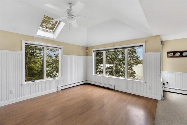 empty room with a healthy amount of sunlight, a wainscoted wall, vaulted ceiling with skylight, and wood finished floors