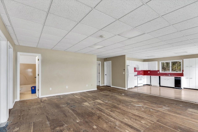 unfurnished living room featuring a drop ceiling, baseboards, dark wood-type flooring, and a sink