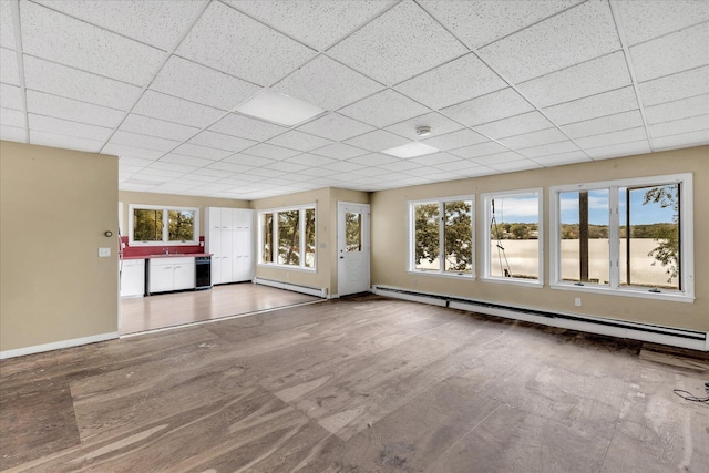 unfurnished living room with a baseboard heating unit, baseboard heating, a paneled ceiling, and baseboards