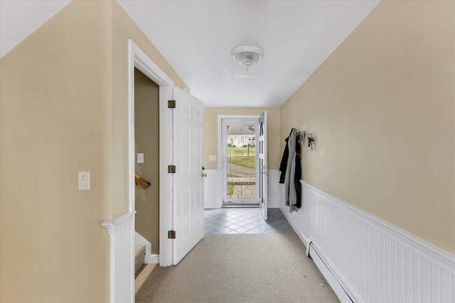 hallway featuring a wainscoted wall, a baseboard radiator, stairs, and light colored carpet