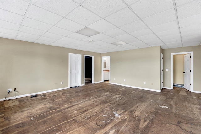 empty room with wood finished floors, a paneled ceiling, and baseboards