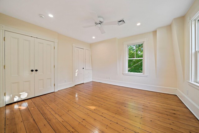 unfurnished bedroom featuring ceiling fan, hardwood / wood-style floors, and two closets