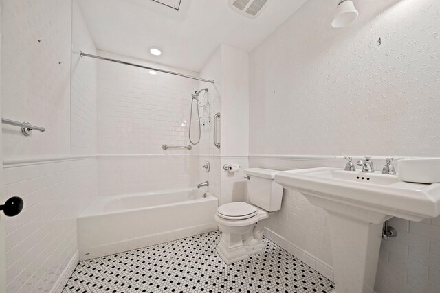 bathroom featuring tile patterned floors, tile walls, toilet, and tiled shower / bath combo