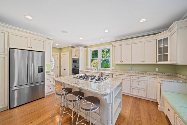 kitchen with appliances with stainless steel finishes, light stone counters, a center island, ornamental molding, and light hardwood / wood-style floors