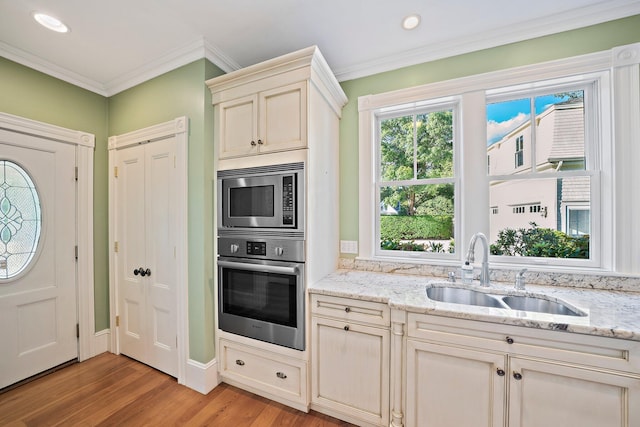 kitchen with sink, cream cabinetry, light wood-type flooring, stainless steel appliances, and light stone counters