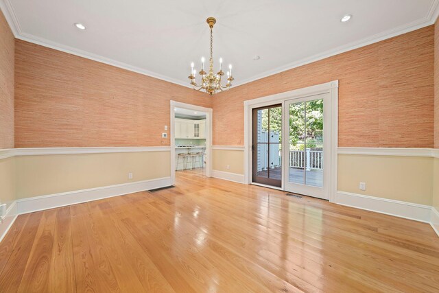 spare room with hardwood / wood-style flooring, ornamental molding, and an inviting chandelier