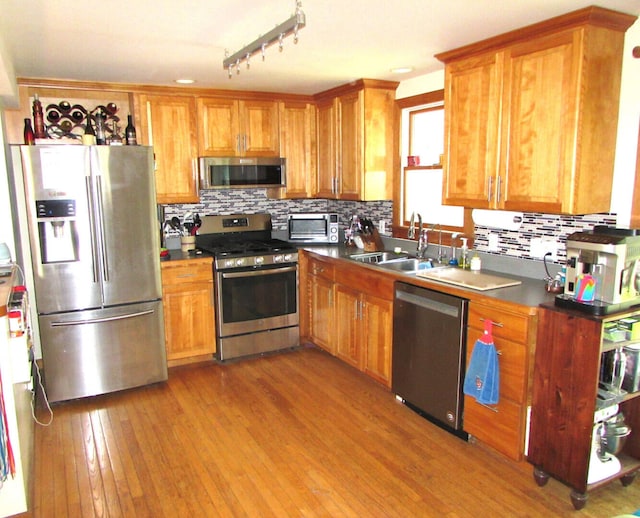 kitchen featuring dark countertops, backsplash, light wood-style flooring, appliances with stainless steel finishes, and a sink