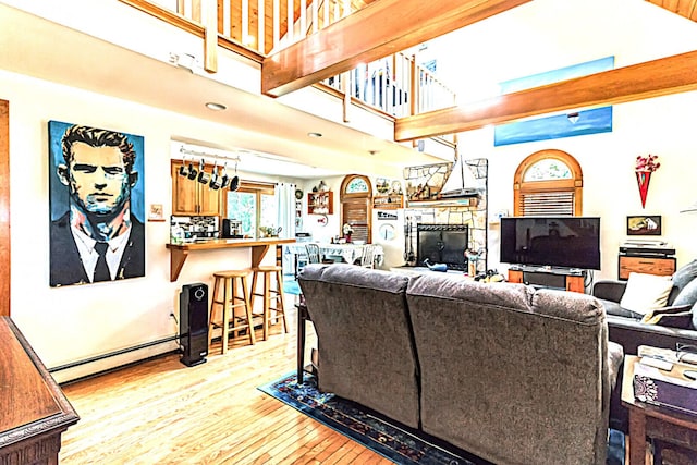 living room with a fireplace, a baseboard radiator, a towering ceiling, and light wood-style flooring