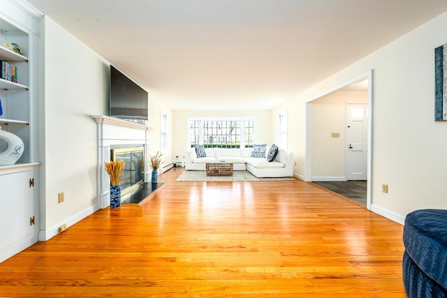 living area featuring wood finished floors, a fireplace with flush hearth, built in shelves, and baseboards