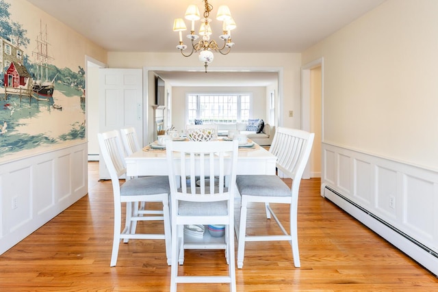 dining area with baseboard heating, a chandelier, light wood-style flooring, wainscoting, and a decorative wall