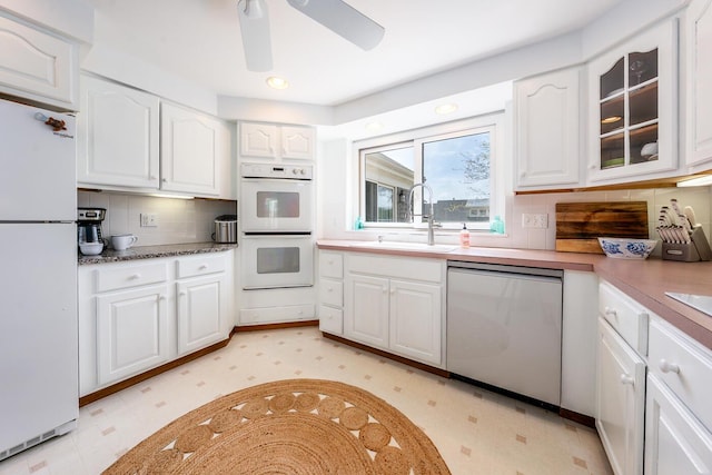 kitchen featuring white appliances, a sink, light flooring, white cabinetry, and a ceiling fan