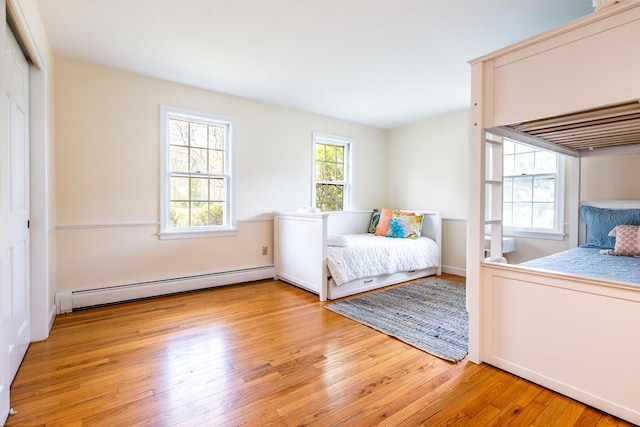 bedroom with a baseboard radiator, light wood finished floors, and a closet