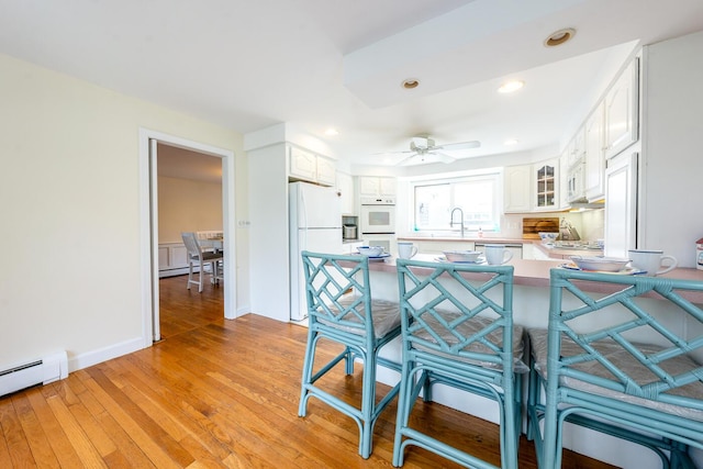 kitchen featuring a kitchen bar, white appliances, a peninsula, glass insert cabinets, and white cabinets