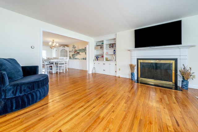 living room with a chandelier, light wood-style floors, a fireplace with flush hearth, and built in features