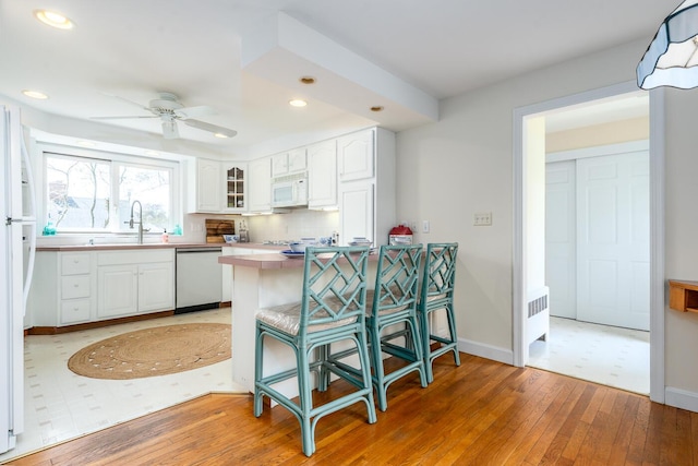 kitchen with white appliances, a peninsula, white cabinetry, a sink, and recessed lighting